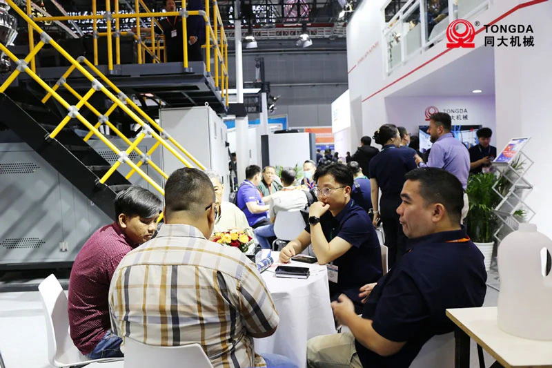 Visiteurs rencontrant l’équipe Tongda près d’une machine de soufflage à CHINAPLAS 2024